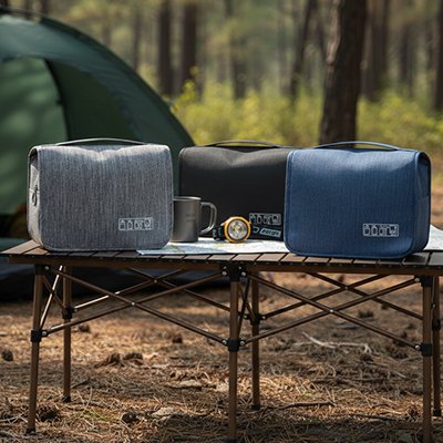 Trousse de toilette homme les trois modèles mises sur une table portable de camping dans une belle forêt