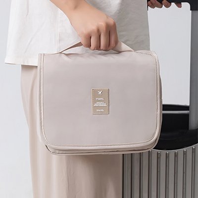 Trousse de toilette voyage beige porté par la poigné