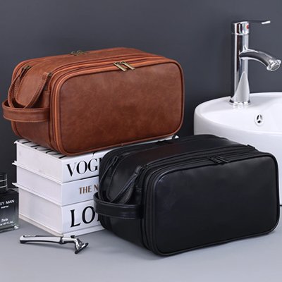 Trousse de toilette voyage effet cuir véritable posée dans une salle de bain moderne, une noir et une marron