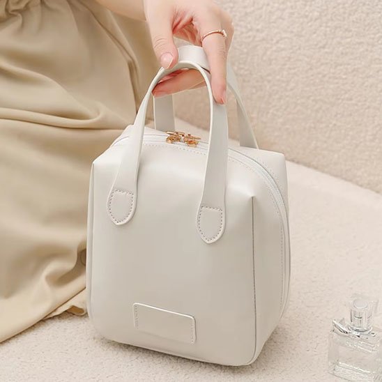 trousse maquillage blanche tenue par la main d'une femme sur table grège et décor épuré 