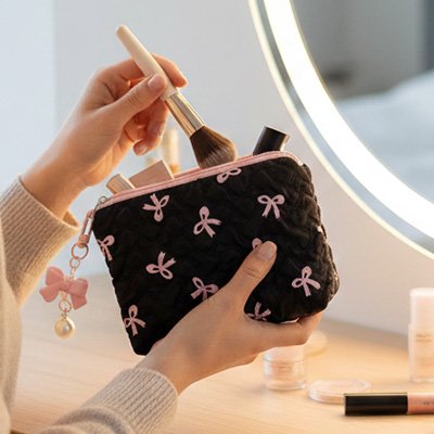 Mini trousse maquillage noir boucle rose dans main d'une femme