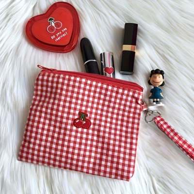 Trousse maquillage rouge à carreaux,  sur un tapis blanc à poils longs, 