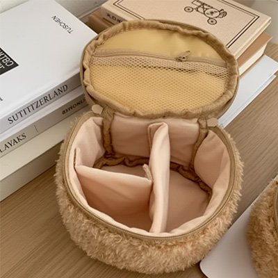 Une trousse à maquillage beige en forme d’ours est ouverte et montre ses compartiments intérieurs. Elle est posée sur un bureau en bois